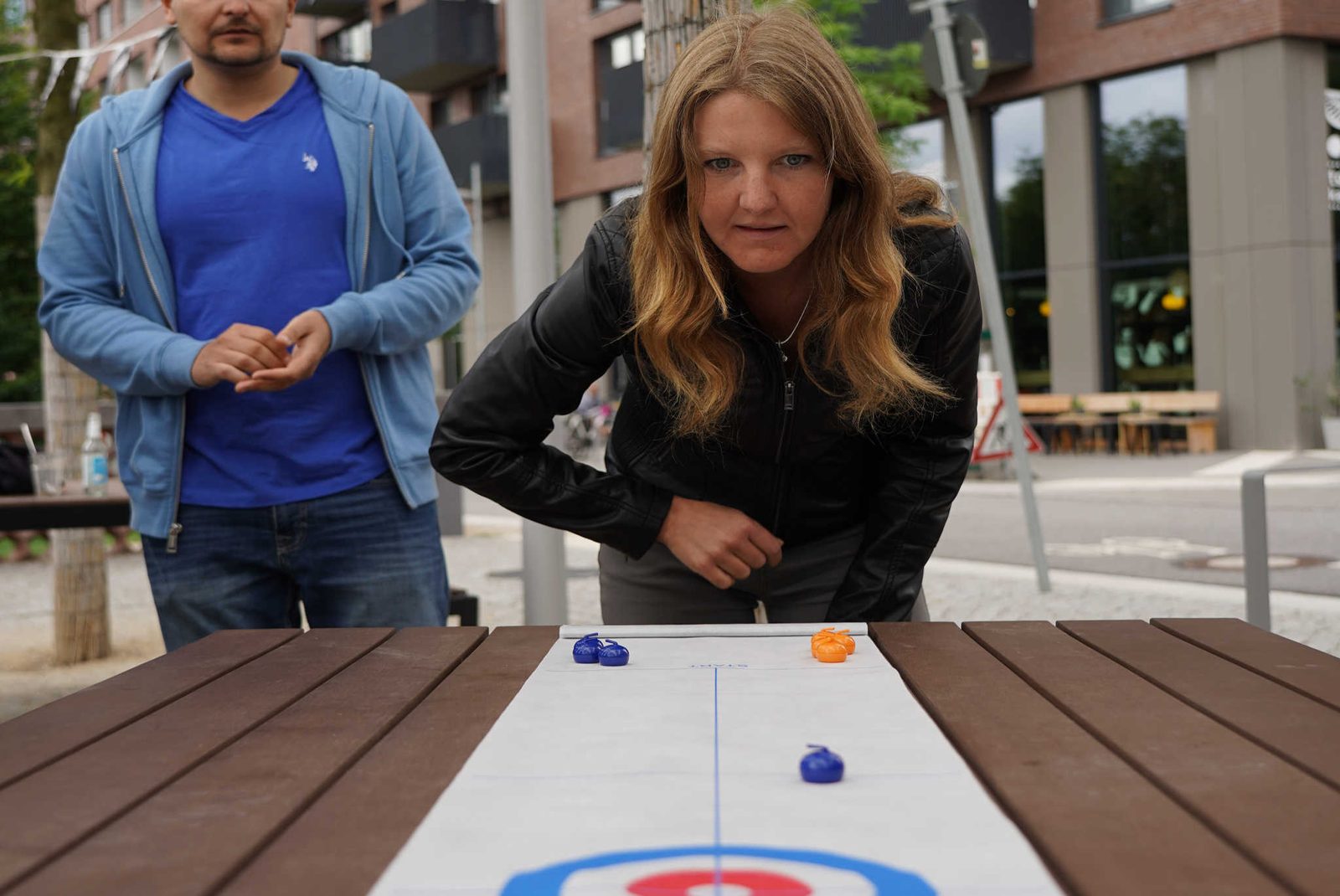 Teilnehmerin zielt konzentriert beim Tischcurling, ein Mitspieler schaut zu